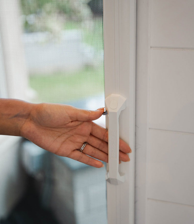 Hand operating thumb latch on white screen door handle