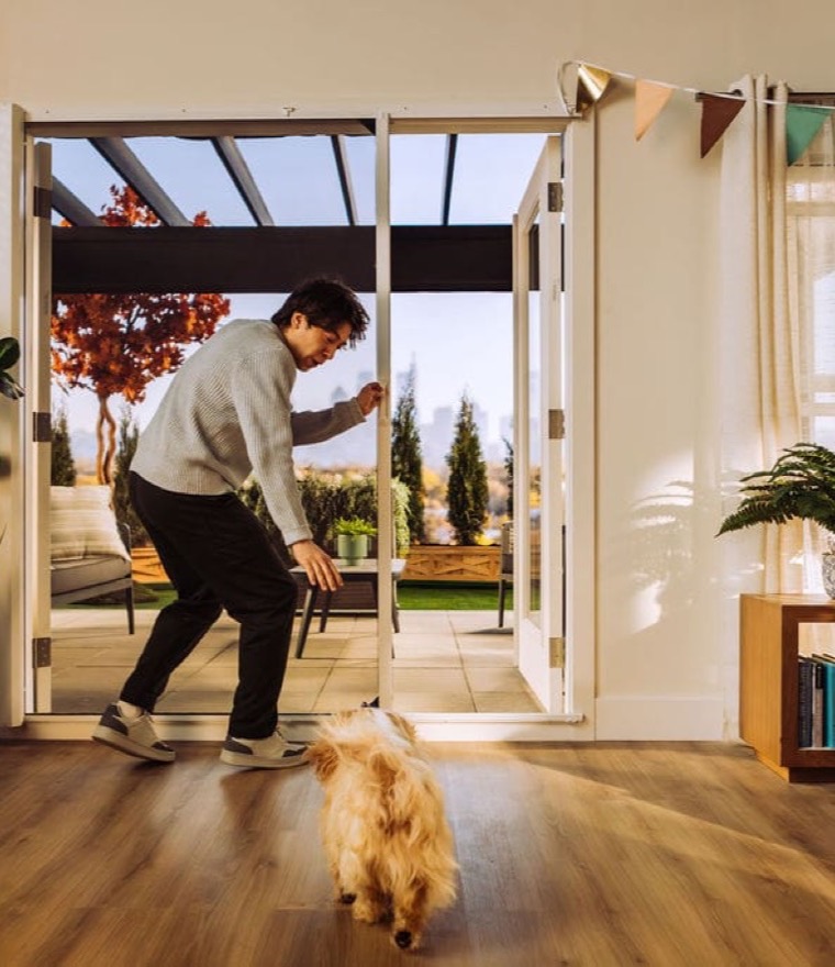 Man playing with a dog at wide-open retractable patio doors leading to a covered terrace, with birthday decorations inside